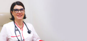 Lekarka Katarzyna Zabłocka siedzi na fotelu, ma na sobie biały fartuch, na szyi stetoskop, uśmiecha się